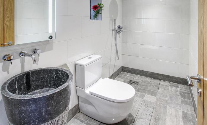 Contemporary bathroom featuring a striking black stone basin, rainfall shower, and sleek white tiling.